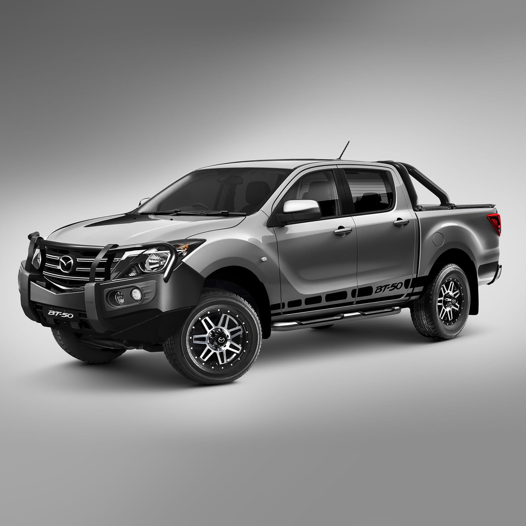 Studio front three-quarter view of a grey Mazda BT-50 dual-cab fitted with a black bull bar, side steps and alloy wheels